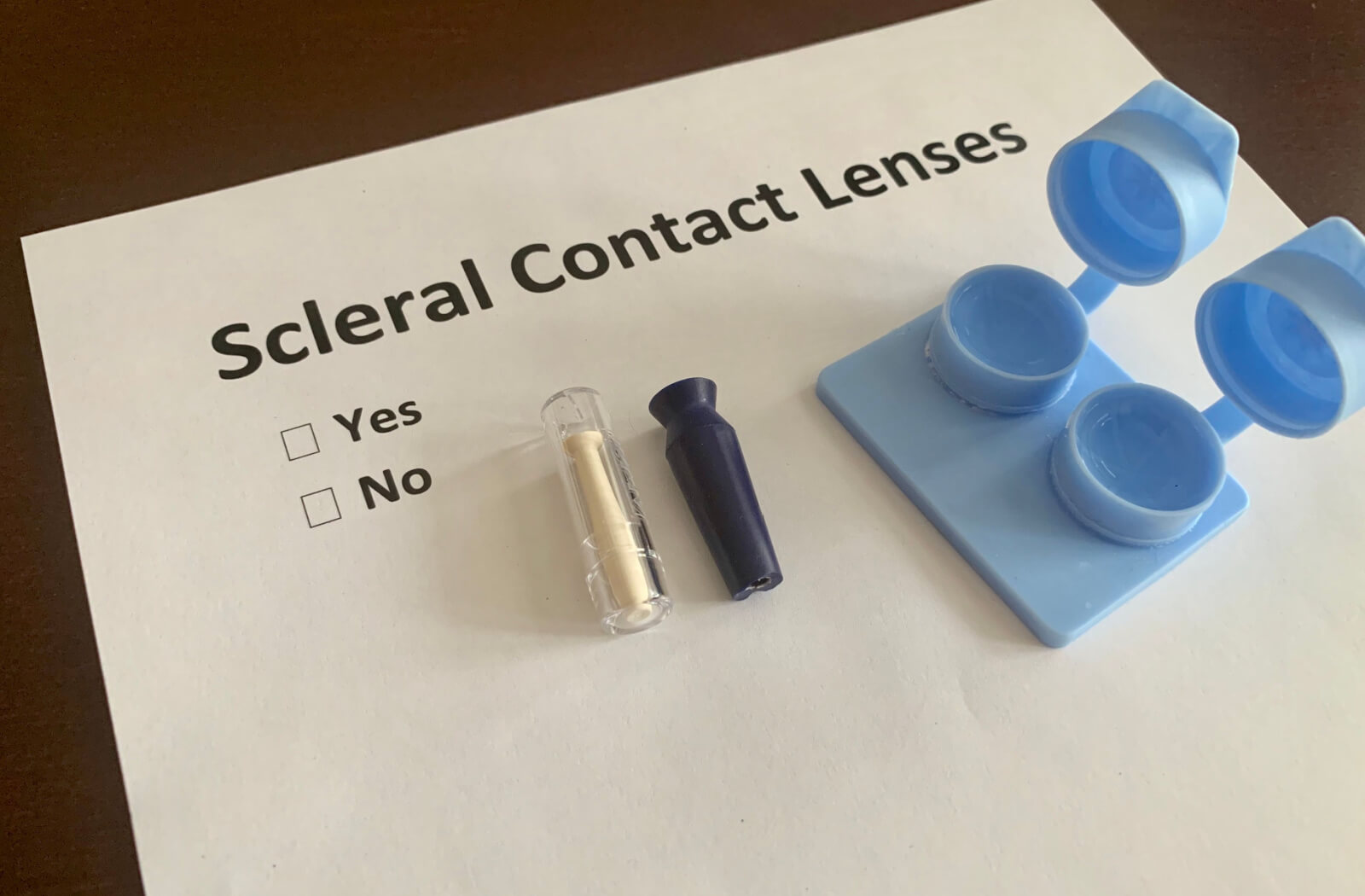 A contact lens case with scleral contacts and a contact lens insertion and removal kit on a piece of paper