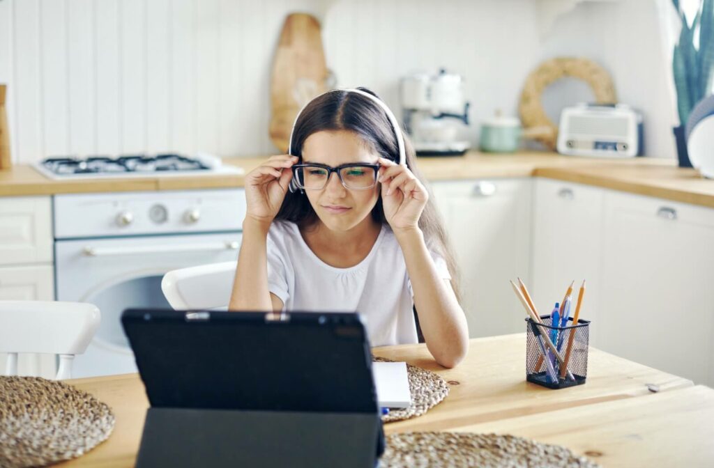 A young girl wearing glasses squints at a computer screen while doing homework.
