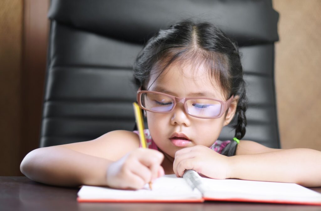 A close-up image of a young girl wearing glasses while carefully writing in a notebook.