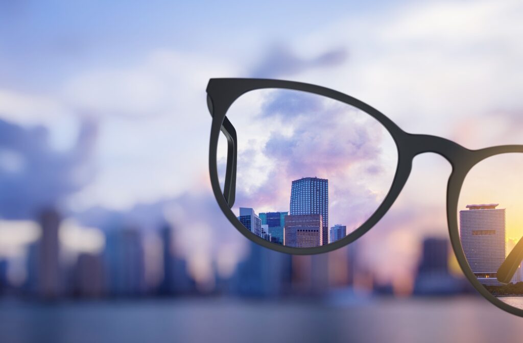 A person holds a pair of glasses up to look at the skyline of a city, with a mountain in the background. The view of the city around the glasses is blurry, while the portions of the city inside the glasses come through clearly.
