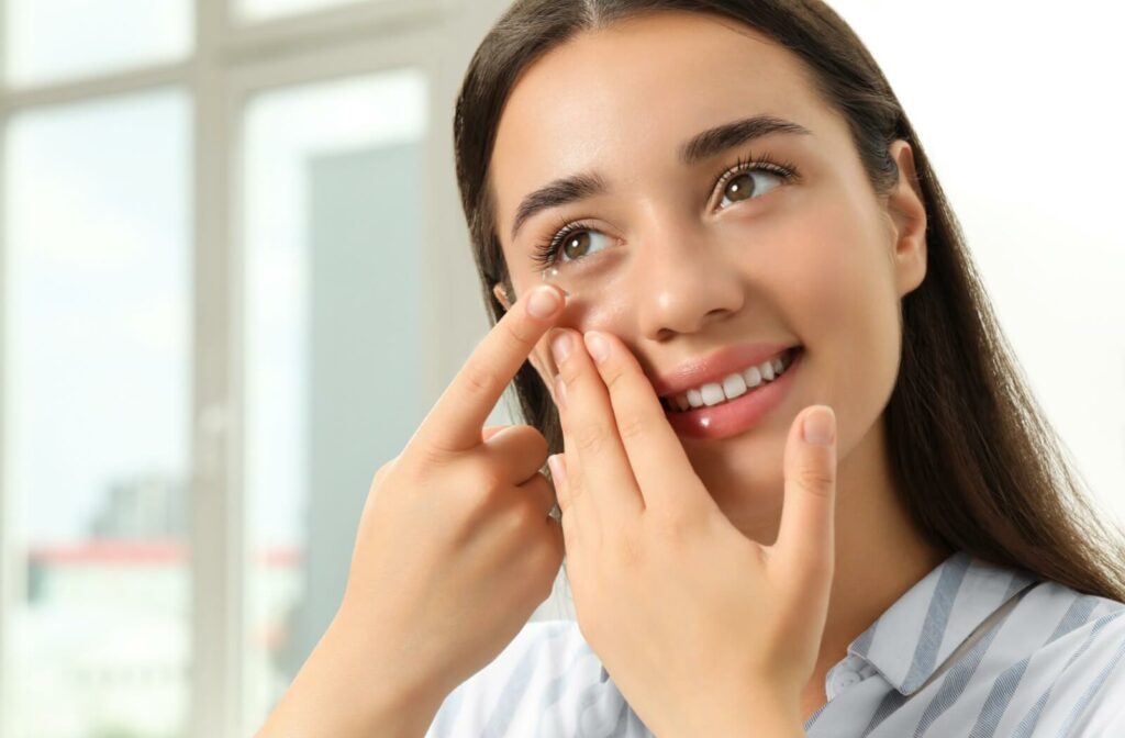 A woman smiling while carefully inserting a scleral lens into her right eye.