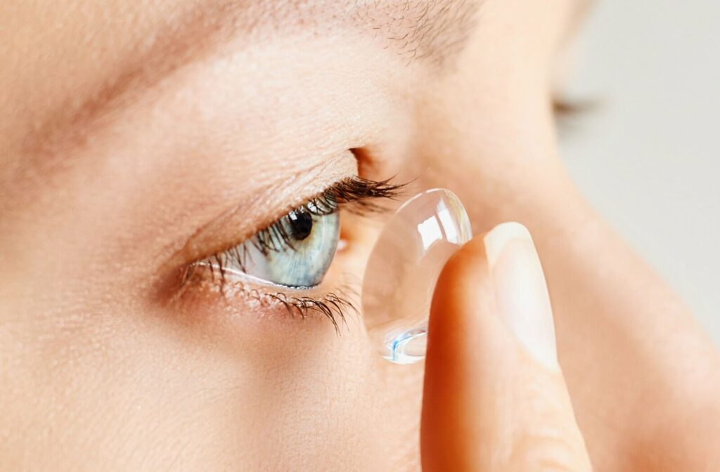 A close-up image of a woman inserting a scleral contact lens into her right eye.