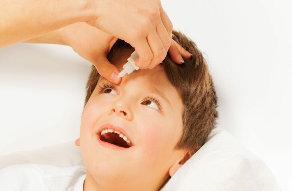 A child laying down while an adult holds their left eyelid open and applying kid-safe eye drops.