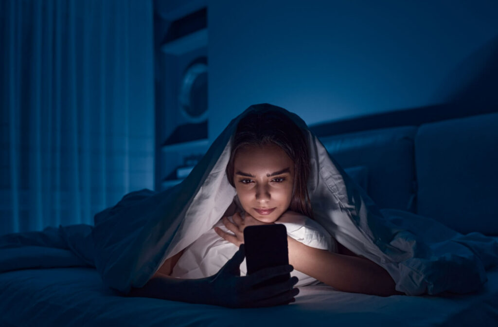 An adult staring at their smartphone in their dark bedroom.