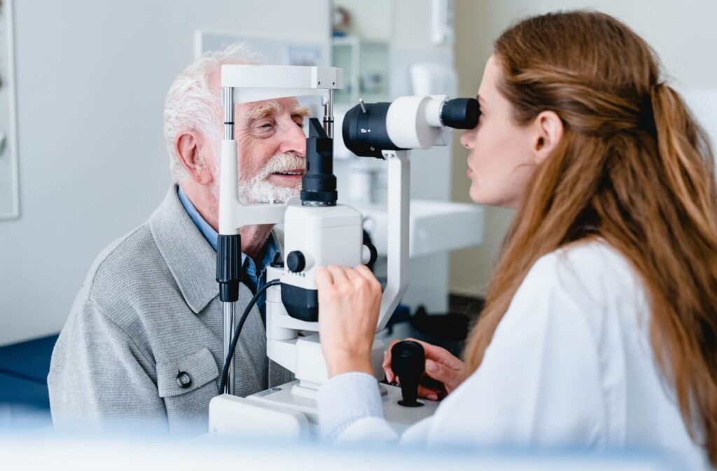 An optometrist carefully examining a smiling older patient's eyes to determine if they need cataract surgery.