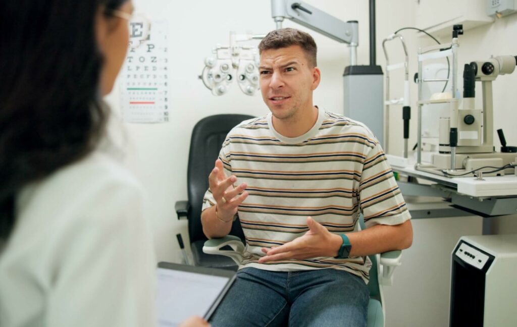 A patient gestures as they explain the symptoms they are experiencing in their eye in detail to their optometrist.