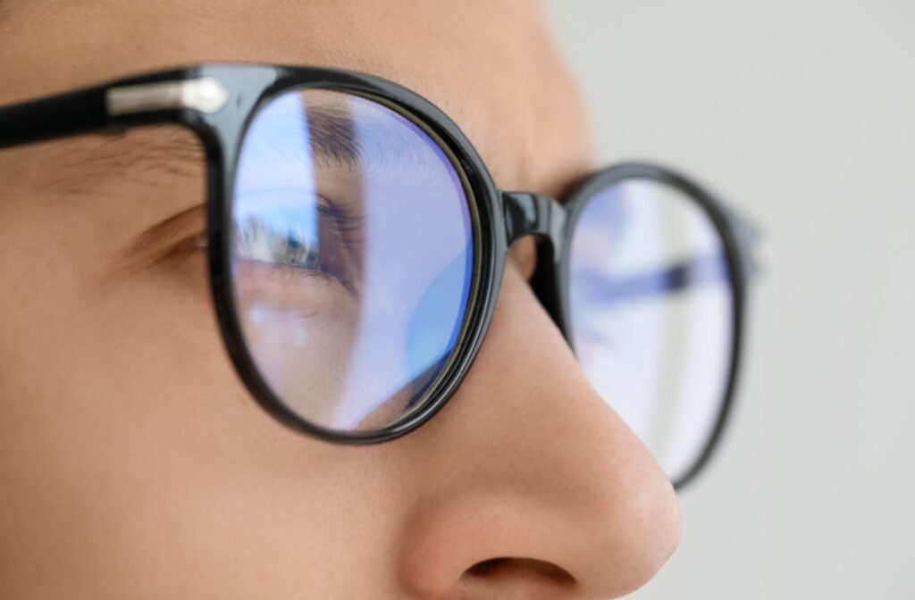Close-up of a person wearing black-rimmed eyeglasses with blue light reflections visible on the lenses.
