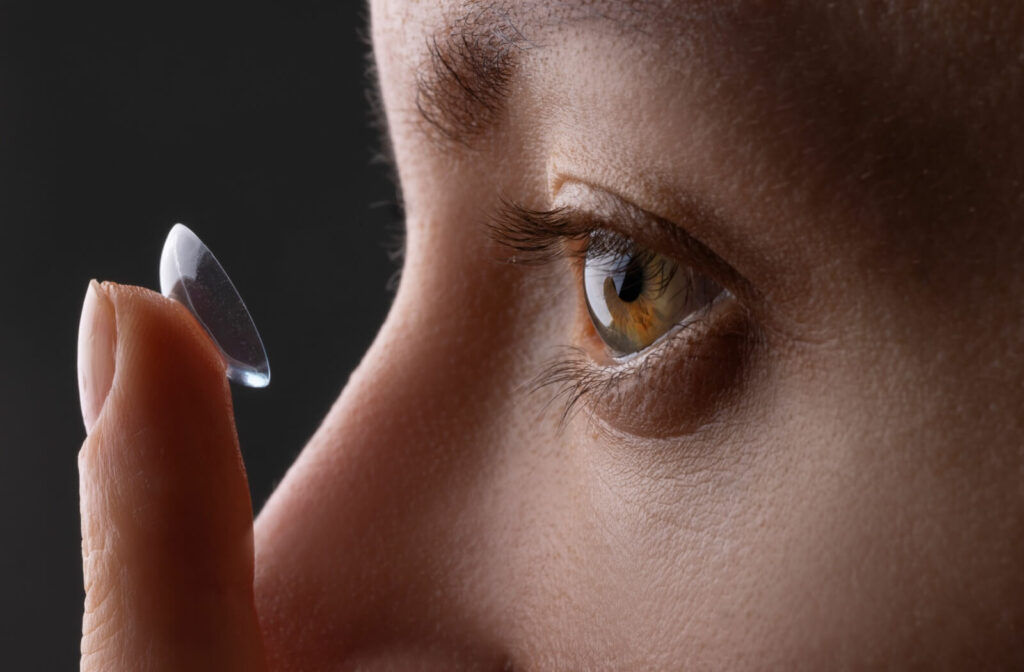 Close-up of a person holding a contact lens near their eye, preparing to apply it.